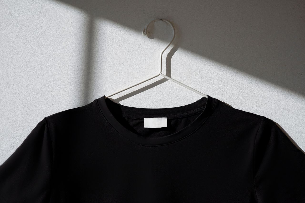 The Art of Drawing Readers In: Your attractive post title goes here Black t-shirt hanging on a white hanger against a plain wall with a dramatic shadow effect.